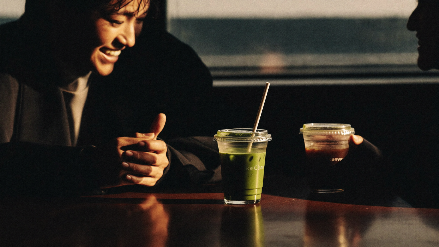 Two friends sharing iced coffee and matcha at a dark café counter